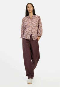 Blomster-mønstret, letvægts button-up skjorte i nuancer af lilla og lyserød, parret med løse, mørkelilla bukser og hvide sneakers.