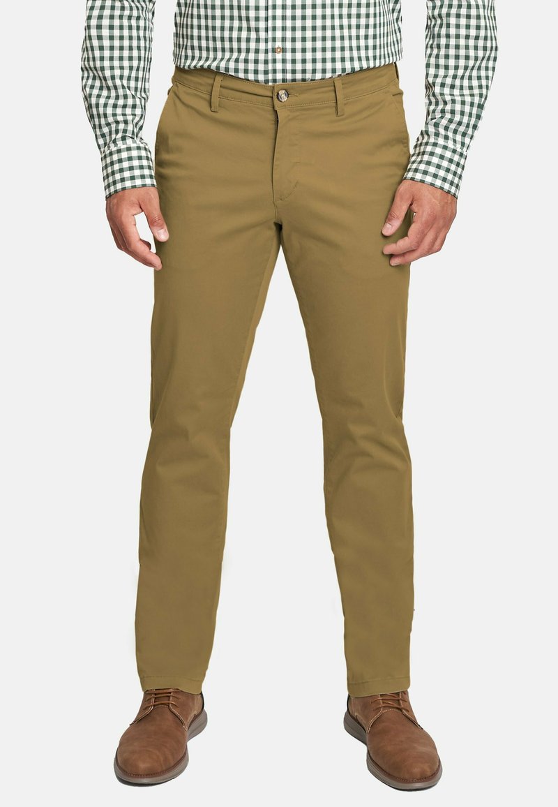 Pantalones de pierna recta en tono beige con una textura suave, diseño de 5 bolsillos y lazos para cinturón, combinados con zapatos marrones y una camisa de cuadros en verde y blanco.