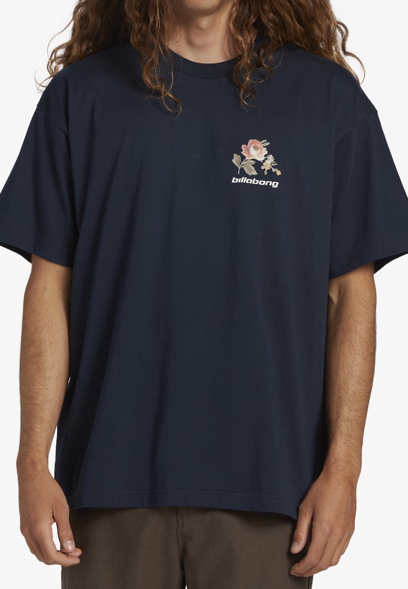 T-shirt en coton bleu marine à manches courtes, avec un motif floral et le logo "Billabong" sur la partie gauche de la poitrine.