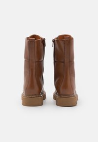 Hnědé kožené kotníkové boty s hladkým povrchem, postranním zipem a texturovanými gumovými podrážkami, se švy na bocích.