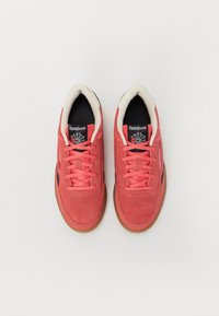 Ténis Reebok em camurça coral com pormenores pretos, apresentando um colarinho acolchoado, atacadores planos e uma solas de borracha de goma para tração.