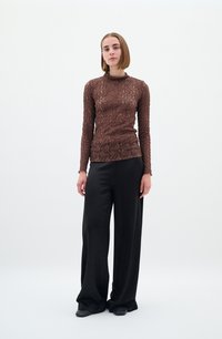 Maglia marrone a maniche lunghe con un design in pizzo testurizzato, abbinata a pantaloni neri larghi, caratterizzati da una finitura liscia e gambe ampie.