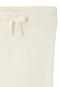 Nahaufnahme von cremefarbenen, gerippten Strickhosen mit einer gebundenen Schleife am elastischen Bund.