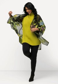 Geel geribbelde tuniek onder een sheer zwarte kimono met bloemenborduursel. Zwarte strakke broek en spitse zwarte hakken maken de outfit compleet.