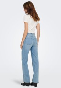 Light blue denim wide-leg jeans with a high waist; visible stitching, two back pockets; paired with a fitted white t-shirt and black heeled boots.