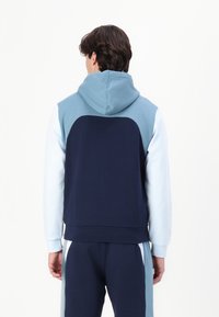 Huvtröja med marinblå kropp, ljusblå ärmar och en strukturerad design. Slät tyg med ribbade muddar och midja.