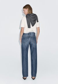 Vit t-shirt, grå scarf över axlarna, blå vida denimjeans, högklackade skor, synliga detaljer på bakfickorna.