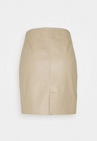 Mini-jupe en similicuir beige avec une taille haute et une fente centrale au dos sur un fond blanc uni.