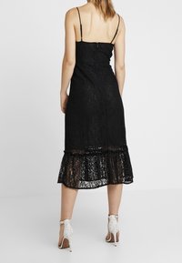 Svart spetsklänning med spaghetti-remmar, åtsittande midja och utfläkt fåll. Har en genomskinlig volang i botten och en dragkedja på baksidan.