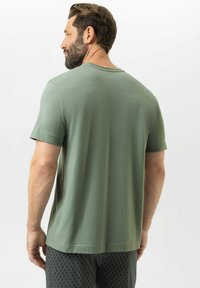 T-shirt vert à manches courtes en tissu doux, avec un col rond et une coupe décontractée ; porté avec un pantalon à motifs noir et blanc.