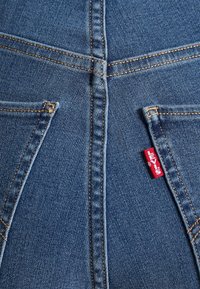 Gros plan de denim bleu avec deux poches arrière et une étiquette rouge de la marque Levi's visible sur la couture de la poche droite.