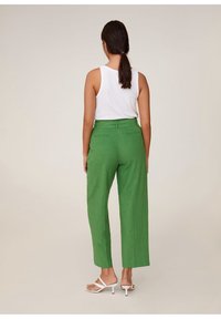 Zelené lněné kalhoty s vysokým pasem, širokými nohavicemi a zadními kapsami, kombinované s bílým topem bez rukávů a bílými sandály.