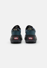 Adidași negri și bleumarin cu o talpă texturată, având un tab anterior cu brand și accente galbene. Design robust pentru utilizare în aer liber.