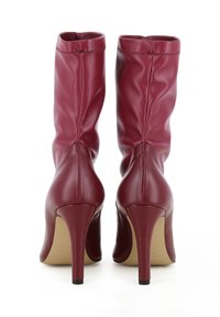 Bottines en cuir bordeaux avec un design ajusté, des talons aiguilles hauts, et des détails de couture subtils le long du bord supérieur.