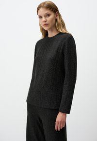 Maglione nero con texture a coste, maniche lunghe e scollo a rotondo. Mostrato con pantaloni coordinati a coste su uno sfondo neutro.