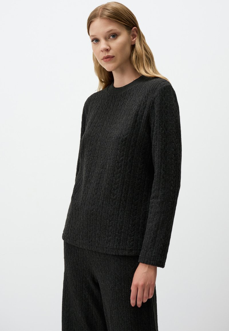 Maglione nero con texture a coste, maniche lunghe e scollo a rotondo. Mostrato con pantaloni coordinati a coste su uno sfondo neutro.
