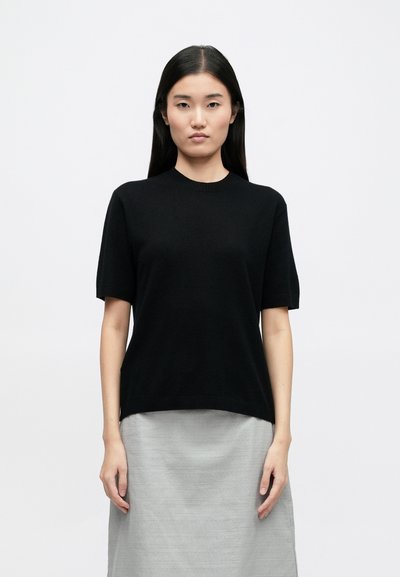 Black short-sleeve knitted top with a round neckline, relaxed fit, and ribbed hem, paired with a light gray textured skirt.