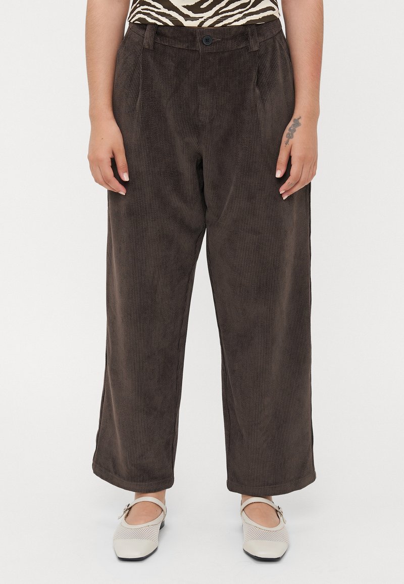 Brune cordfløyelsbukser med bred ben design, som har frontfolder, sidelommer og en knappeåpning i livet.