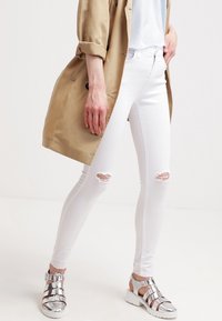 Vita smala jeans med slitna knäpartier, kombinerade med silverfärgade metalliska sandaler med utskurna detaljer och en kraftig vit sula.