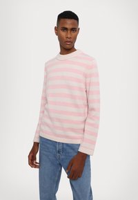 Svetar z rožnatimi in belimi črtami, pleten z okroglo izrezom in dolgimi rokavi, v kombinaciji z modrimi kavbojkami. Gladka tekstura, sproščen dizajn.