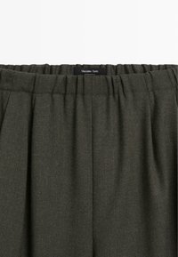 Pantaloni plissettati verde scuro realizzati in tessuto testurizzato, con vita elastica e un'etichetta nera con la scritta "Massimo Dutti."