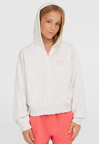 Lys grå zip-up hættetrøje med en blød tekstur, der har et lille pink hjerte-logo på brystet. Akkompagneret af koralfarvede shorts.