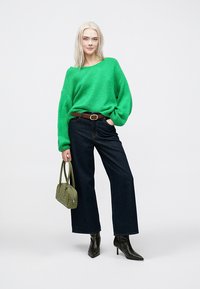 Πράσινο φαρδύ πλεκτό πουλόβερ, σκούρο ψηλόμεσο παντελόνι με φαρδιά πόδια, μαύρες μυτερές μπότες μέχρι τον αστράγαλο και μια μικρή ελαιόχρωμη τσάντα ώμου.