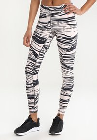 Tights i stretchtyg med rosa bas och svart abstrakt randmönster, tillsammans med svarta sportskor.