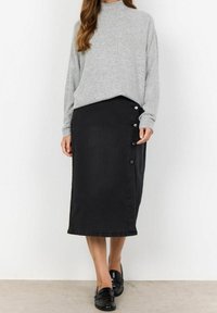 Sort denimnederdel med en mellemlang design, prydet med sidelukninger; sammen med en grå, løs sweater og sorte loafers.
