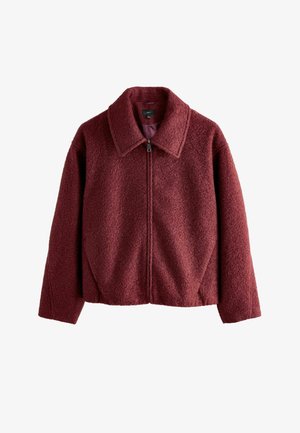 Veste en polaire bourgogne avec un col, fermeture éclair et tissu texturé. Présente une coupe décontractée et des détails de couture visibles.