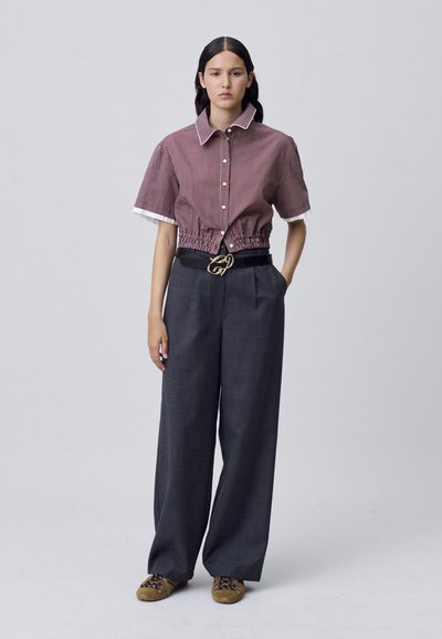 Camisa corta de cuadros rojos y blancos con mangas cortas y dobladillo elástico, combinada con pantalones de pierna ancha oscuros y un cinturón negro con herrajes dorados.