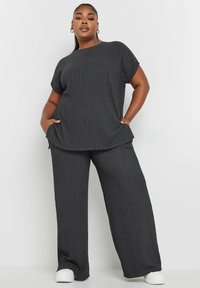 Tummanharmaa kaksiosainen asu, johon kuuluu lyhythihainen paita, jossa on tekstuuri, ja leveälahkeiset housut, valmistettu pehmeästä ja joustavasta materiaalista.