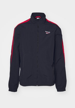 Melnas sporta jakas ar sarkaniem sānu svītrām, ar rāvējslēdzēju un stenda apkakli. Augšējā kreisajā krūtī atrodas Reebok logo. Viegls materiāls.