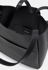 Czarna skórzana torba tote o gładkiej teksturze, z kieszenią wewnętrzną i zapięciem na zatrzask. Posiada krótkie uchwyty, które ułatwiają noszenie.