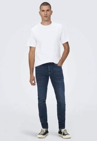 Bijela kratka majica s kratkim rukavima, krojena, u kombinaciji s tamnoplavim uskim trapericama. Crne niske tenisice upotpunjuju izgled. Jednostavan i svakodnevni dizajn.