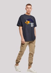 Marine bomulls T-skjorte med grafikk av en tegneserie-fugl og teksten "BEEP, BEEP." Kombinert med khaki cargo-bukser og hvite sneakers. Behagelig passform.