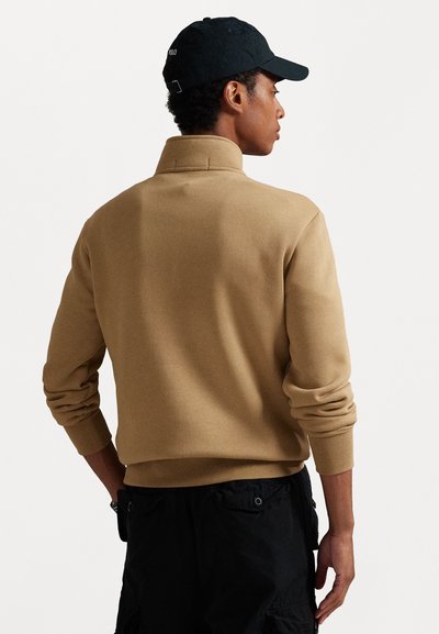 Khaki värvi sv sweatshirt koos ribaga kaeluse ja varrukate ning lõdva istuvuse ja tekstuuriga kangaga, kantud mustade cargo pükstega.