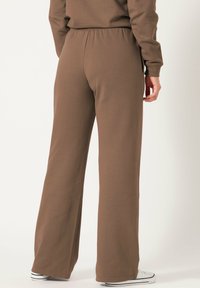 Pantalons de survêtement en coton marron avec une coupe décontractée, une taille élastique et des jambes évasées. Le tissu a une texture lisse et un minimalisme dans ses détails.