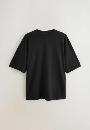 Camiseta negra de manga corta confeccionada en algodón, con cuello redondo y corte holgado. Textura suave sin patrones o detalles visibles.