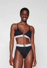 Melns bikini komplekts ar trīsstūrveida augšu un augstu vidukli apakšā. Dizainā ir balta svītraina josla ar priekšpuses logotipa detaļu. Gluda tekstūra.