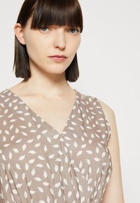 Braunes ärmelloses Kleid mit einem V-Ausschnitt und einem weißen Blattmuster, aus weichem Stoff mit glatter Textur.