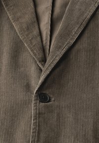 Blazer de pana en marrón apagado, con rayas verticales, un solo botón negro y un interior suave. Las solapas estructuradas añaden detalle.