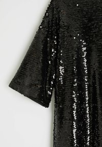 Czarny top z cekinami, z krótkimi rękawami, luźnym krojem i gładką teksturą. Cekiny odbijają światło, tworząc błyszczący efekt.