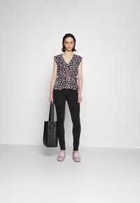 Blusa estampada com flores e mangas de babado, combinada com jeans skinny pretos e sandálias plataforma lilás. Acompanhada de uma mala de tote preta.