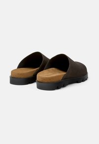 Mörkbruna mockasklipp-sandaler med en tanfärgad dämpad innersula och en svart texturerad gummisula. Öppen baksidan, lågprofilig form.