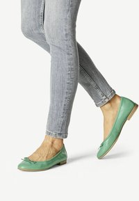 Ballet flats in pelle verde con tacco piatto, caratterizzate da un piccolo fiocco sulla punta, indossate con jeans skinny blu chiaro.