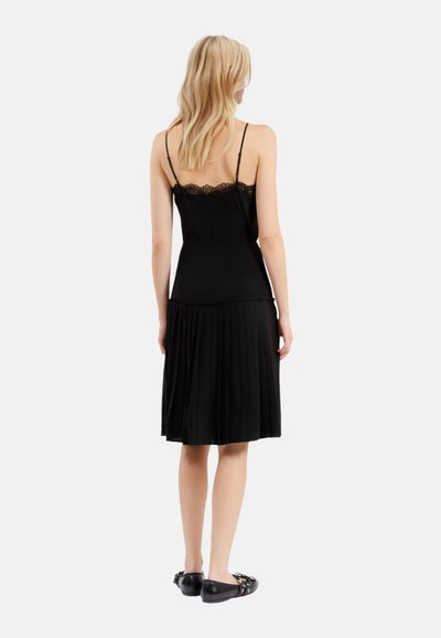 Vestito nero a pieghe con bordo in pizzo sulle spalline, busto aderente e gonna fluida. Il materiale è liscio, con una leggera lucentezza.