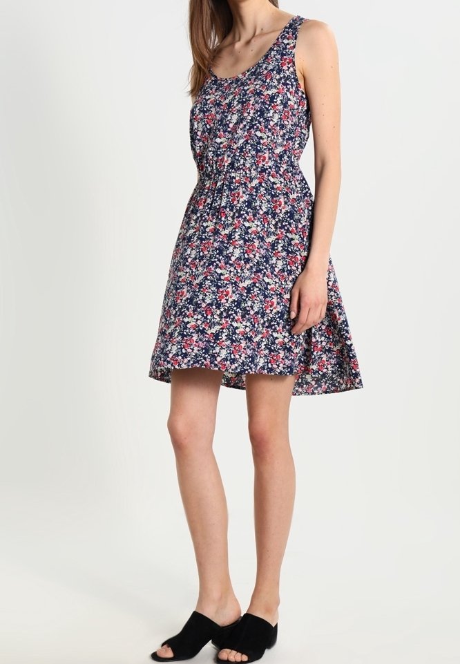 Robe fleurie avec un fond marine, décolleté rond et sans manches. Le tissu est léger et présente de petits motifs floraux multicolores.