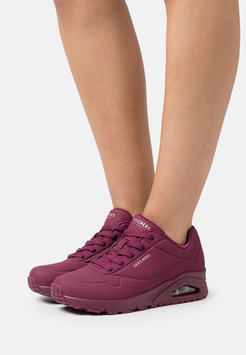 Paire de baskets Skechers violettes avec semelles à coussin d’air visibles, portées sur des jambes nues sur un fond blanc uni.