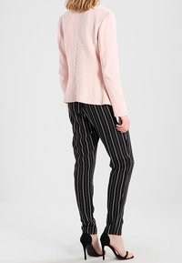 Svetle růžový dlouhý rukáv top s rovnou siluetou, sladěný s černými pruhovanými kalhotami se slim fit střihem a vysokými černými sandály.
